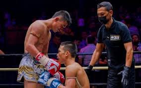 Combattant à genoux dans le ring sous le regard de l'arbitre