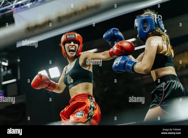 Deux boxeuses en action dans un ring, casques rouge et bleu